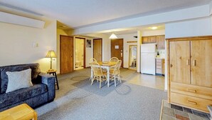 Una sala de estar con sofá, una mesa de comedor con sillas, una zona de cocina y un mueble de madera.