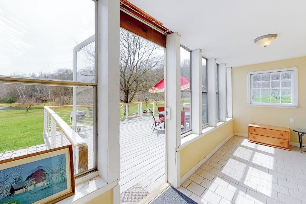 Une pièce dotée de grandes fenêtres, d’une terrasse en bois et offrant une vue sur un paysage verdoyant.