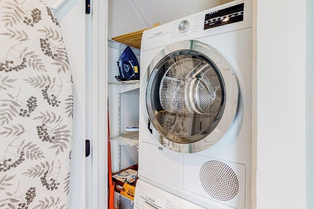 Une machine à laver à chargement frontal dans une buanderie, avec des étagères et un rideau à motifs.