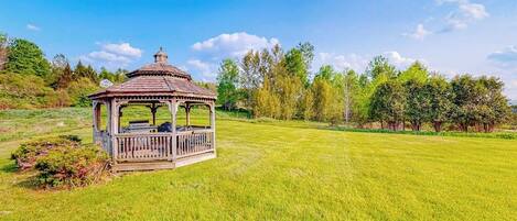 A gazebo in a grassy field with trees in the background.