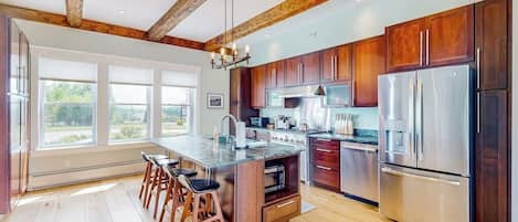 Una cocina amplia con vigas de madera, una isla grande y electrodomésticos de acero inoxidable.