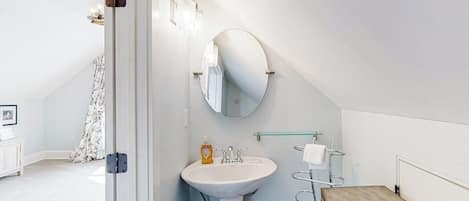 A bathroom with a white sink, a round mirror, and a towel rack.