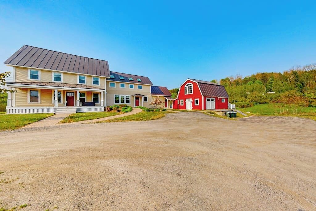 A two-story house with a red barn, a driveway, and a grassy area.