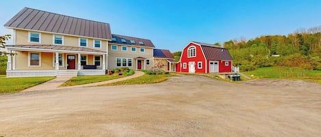 A two-story house with a red barn, a driveway, and a grassy area.