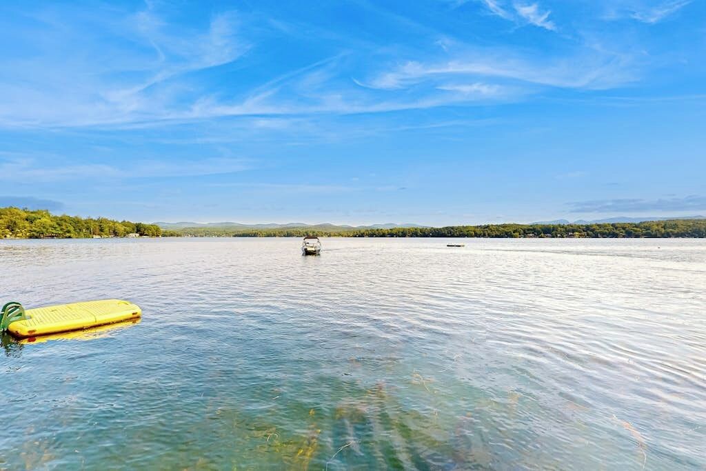 Un lago calmo con un galleggiante giallo in primo piano e una costa lontana con alberi.