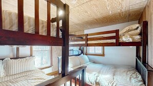 Een slaapkamer met een stapelbed, houten leuningen en een schuine kap.