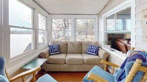 Een gezellige kamer met een beige bank, twee blauwe kussens, een houten stoel en een klein tafeltje.