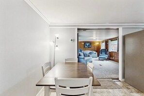 Ein Essbereich mit Holztisch und weißen Stühlen, der in ein Wohnzimmer mit blauem Sofa und Fernseher übergeht.