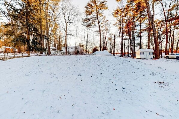 A snow-covered yard with trees and a small white building. - Single-level Lake Bomoseen home with fenced yard and shared tennis courts (Castleton)