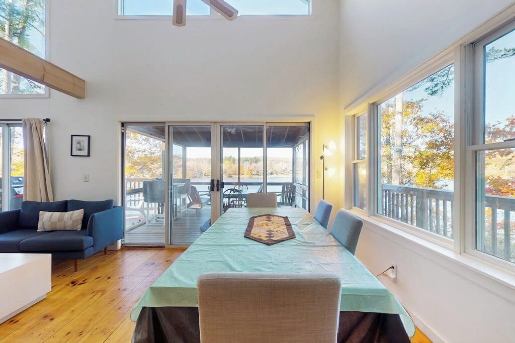 Une pièce spacieuse avec une longue table, un canapé et de grandes fenêtres donnant sur l’extérieur.