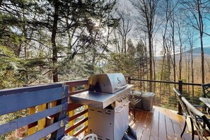 Eine Terrasse mit Grill, einer Sitzbank und Blick auf einen bewaldeten Bereich.