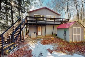Ein zweistöckiges Haus mit überdachter Veranda, einem kleinen Schuppen und einer Treppe, die zum oberen Stockwerk führt.
