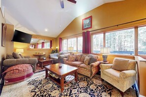 Ein Wohnzimmer mit Sofa, Sessel, Couchtisch und einem Flachbildfernseher.