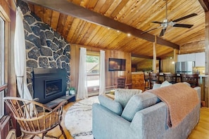 Ein gemütliches Wohnzimmer mit Kamin aus Stein, Holzbalkendecke und einer großen Couch.