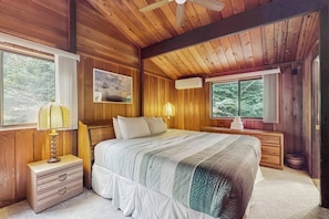 Ein Schlafzimmer einer Holzhütte mit Bett, Nachttischen, Deckenventilator und Fenstern.
