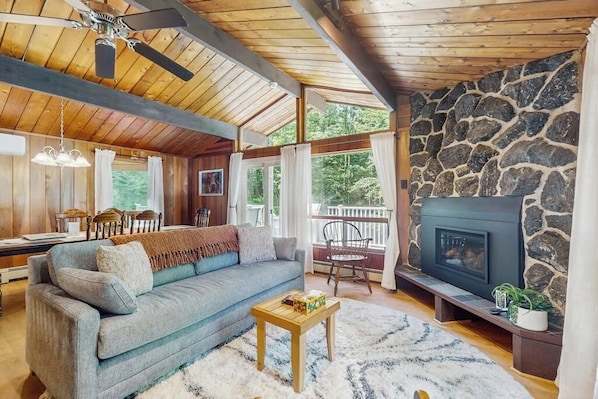 Ein gemütliches Blockhauss-Interieur mit Kamin, einer Couch, einem Esstisch und einem Deckenventilator.