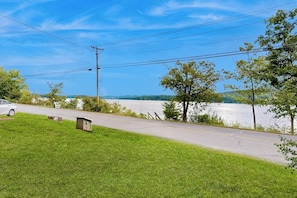 A road with a grassy area, a small shed, and a body of water in the background. - Cozy home with lake front property, views, bbq, dock, kayak, wifi, TV, w/d (Castleton)