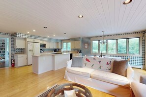 Eine moderne Küche mit weißen Schränken, einer zentralen Kochinsel und einem Essbereich mit einem weißen Sofa.