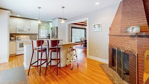 A modern kitchen with white cabinets, a central island, and a brick fireplace. - Lakefront house with mountain-range views, waterfront dock, 2 SUPs & kayak (Castleton)