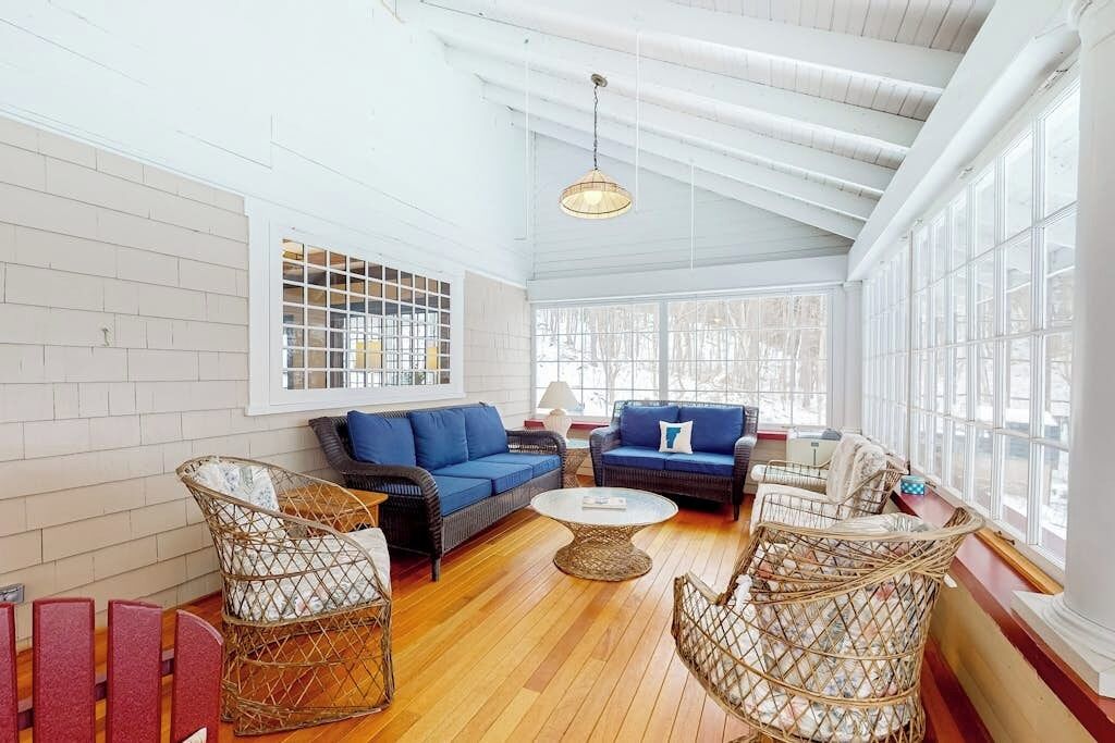 Una habitación con techo alto, ventanas amplias, muebles de mimbre y un sofá azul.