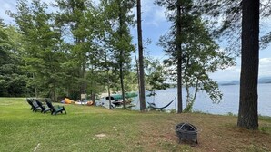 A grassy area with a hammock, chairs, and a fire pit near a lake. - Lakefront house with mountain-range views, waterfront dock, 2 SUPs & kayak (Castleton)