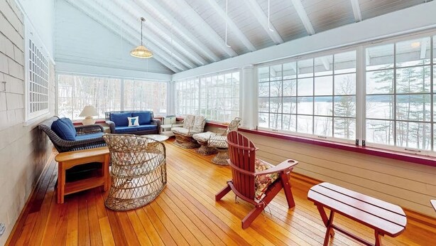 A sunlit room with wooden floors, a blue sofa, wicker chairs, and a wooden bench. - Lakefront house with mountain-range views, waterfront dock, 2 SUPs & kayak (Castleton)