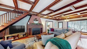 A living room with a fireplace, a television, a staircase, and a large window. - Lakefront house with mountain-range views, waterfront dock, 2 SUPs & kayak (Castleton)