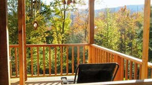 Um deck de madeira com uma cadeira, cercado por guarda-corpo, com vista para uma área arborizada.