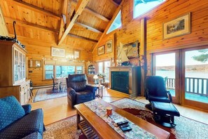 Ein Interieur einer Holzhütte mit Kamin, Ledersesseln, einer Couch und einem Esstisch.