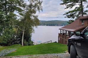 Eine Hütte mit einer Terrasse mit Blick auf einen See, ein Fahrzeug davor geparkt, und freie Sicht auf das Wasser.
