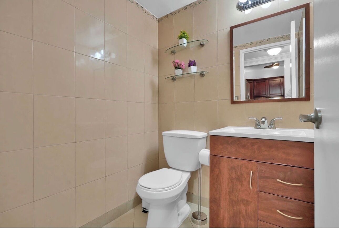 A bathroom with a toilet, a sink, wooden cabinets, and a mirror.