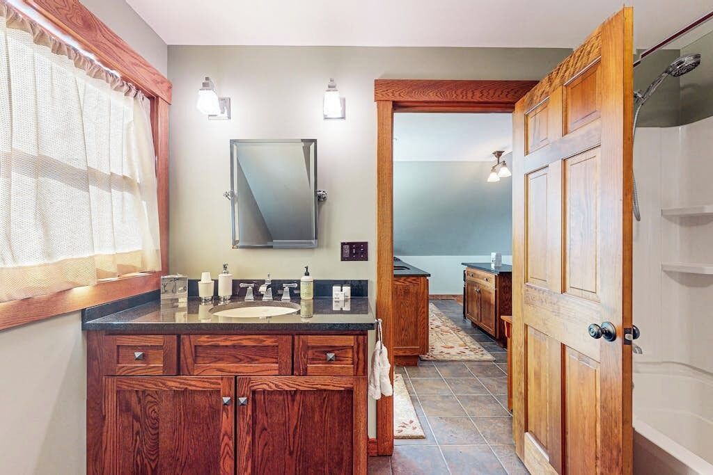 A bathroom with wooden cabinets, a mirror, a sink, and a shower area.