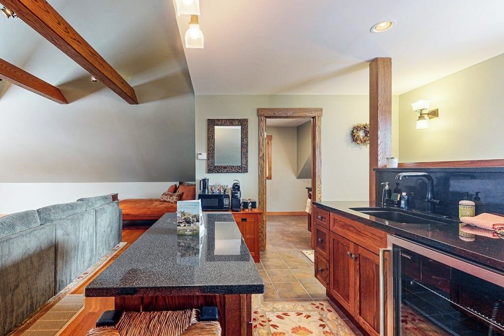 A modern kitchen with wooden cabinets, a granite countertop, and a dining area with a sofa and rug.