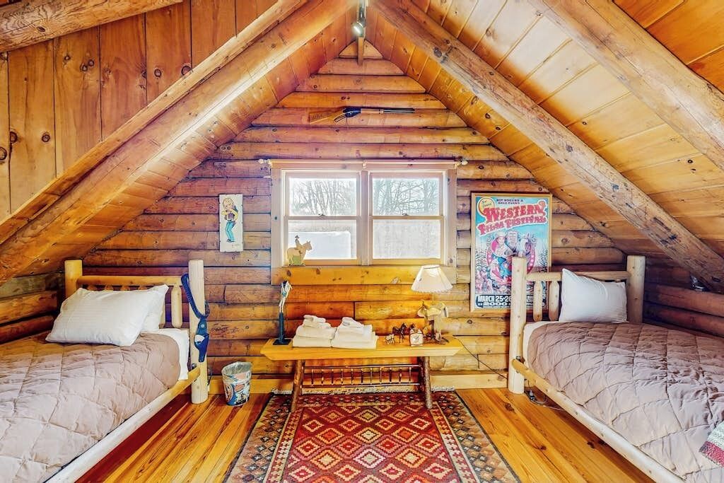 A log cabin room with two beds, a window, a wooden bench, and a poster on the wall.