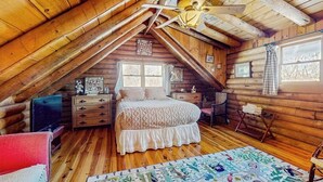 Een slaapkamer in een blokhut met een bed, een dressoir en een plafondventilator.