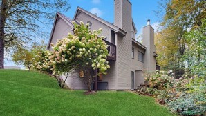 A two-story house with a sloped roof, a chimney, and a well-maintained lawn.