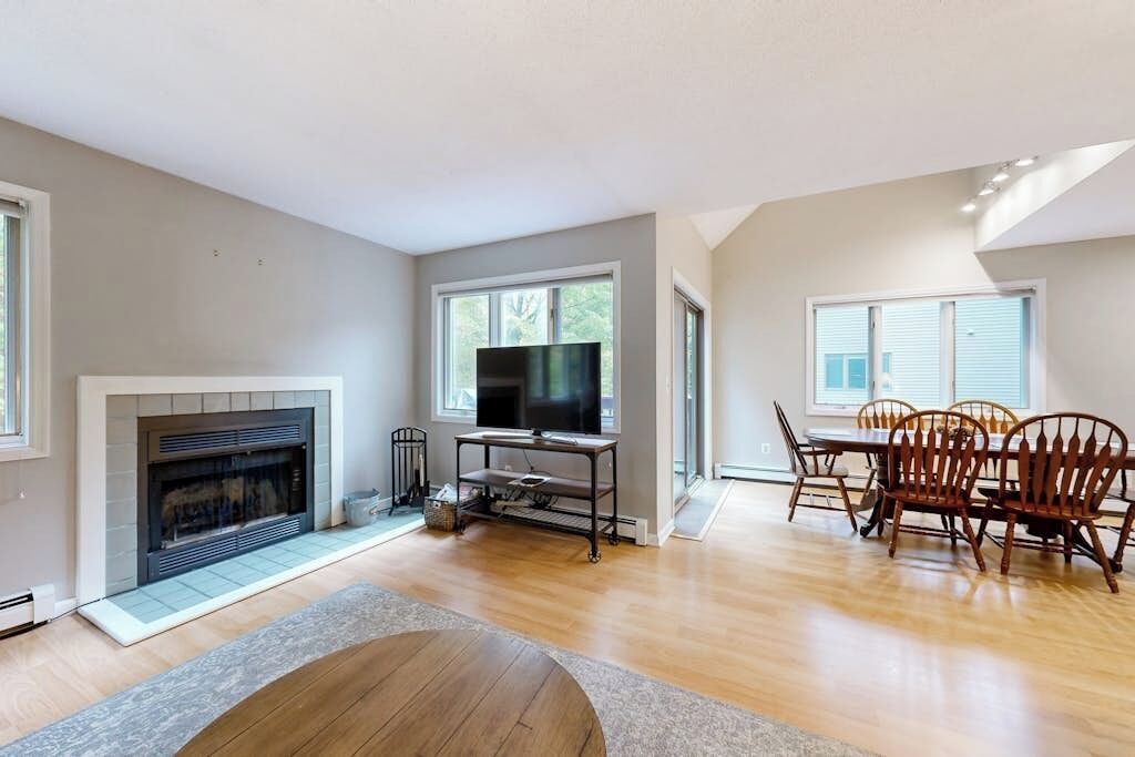 A modern living room with a fireplace, a television on a stand, and a dining area with wooden chairs.