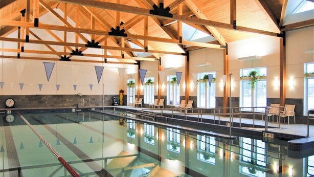 An indoor swimming pool with wooden beams, clear lanes, and lounge chairs.