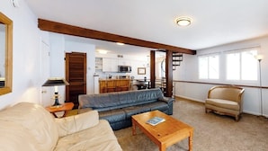 Una sala de estar con un sofá, una mesa de centro de madera, una silla y una cocina al fondo.