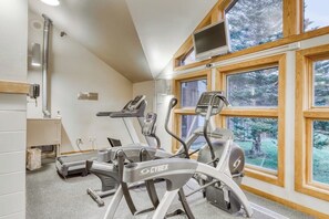 A gym with treadmills, a stationary bike, and a TV mounted on the wall. - First-floor condo with indoor pool, hot tub, fitness room, & game room (Killington)