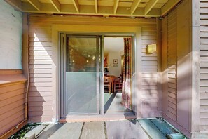 A house with a sliding glass door leading to a porch with a wooden bench and a table. - First-floor condo with indoor pool, hot tub, fitness room, & game room (Killington)