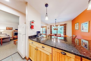 A kitchen with wooden cabinets, a granite countertop, a refrigerator, and a coffee maker. - First-floor condo with indoor pool, hot tub, fitness room, & game room (Killington)