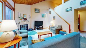 Un salon avec un plafond en bois, une télévision, un canapé, une table basse et un escalier.