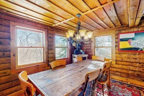 Ein Holzblock-Interieur mit einem Esstisch, Stühlen, einer Kandelaber und großen Fenstern.