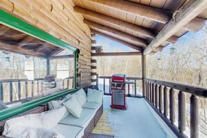 Ein überdachter Außenbereich mit Holzterrasse, einem roten Grill und einer Couch mit Kissen.