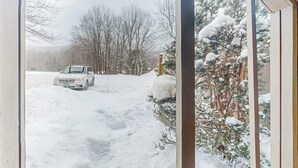 En snötäckt utomhusscen med en bil parkerad i snön, ett trästaket och ett snötäckt träd.