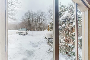 Eine verschneite Winterlandschaft mit einem im Schnee geparkten Auto, einem Holzzaun und einem mit Schnee bedeckten Baum.