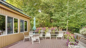 En träveranda med vita metallstolar och -bord, omgiven av frodig grönska och blommande växter.