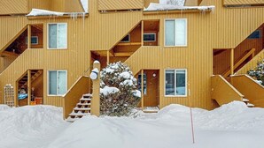 En flervåningsbyggnad av trä med balkonger, en trappa och snö som har samlats på taket.