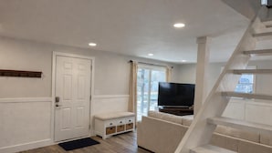 Una sala de estar con sofá, televisión y una escalera.